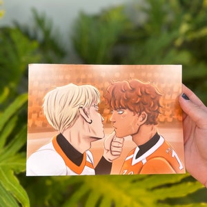 May include: A print of two men in orange and white jerseys looking at each other. The man on the left has blonde hair and the man on the right has brown hair. The background is a blurred image of a crowd.