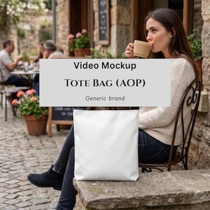 May include: A white tote bag, with the text "Video Mockup TOTE BAG (AOP) Generic brand", sits on a stone surface. A person is seated nearby, holding a cup. The background shows a cafe setting with people and plants.