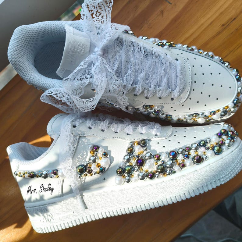 Puede incluir: Zapatillas blancas adornadas con perlas y pedrer&iacute;a iridiscente. Los cordones est&aacute;n adornados con encaje blanco. El texto "Mrs. Shelby" est&aacute; impreso en el lateral. Un dise&ntilde;o de calzado &uacute;nico y decorativo.