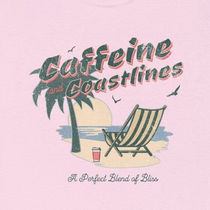 May include: A pink t-shirt with a vintage-style graphic design featuring a palm tree, beach chair, and a cup of coffee. The text reads "Caffeine and Coastlines" and "A Perfect Blend of Bliss".