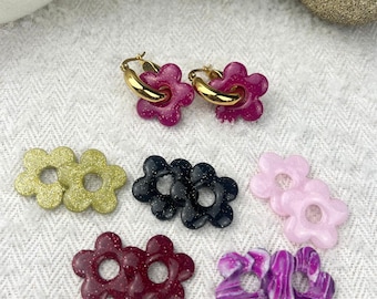 Könnte beinhalten: Ein Set mit sechs Paaren blütenförmiger Ohrringe in verschiedenen Farben, darunter Pink, Lila, Schwarz, Gold und Grün. Die Ohrringe sind aus Glitzer gefertigt und haben ein Loch in der Mitte.