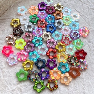 Peut inclure: Une collection de breloques en résine en forme de fleurs avec des accents de paillettes. Les breloques sont de différentes couleurs, notamment le rose, le bleu, le vert, le rouge et le violet. Elles sont parfaites pour ajouter une touche de fantaisie à vos bijoux, vos créations et autres projets.