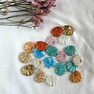 Peut inclure: Assortiment de 16 breloques coquillages irisées de différentes couleurs, dont le rose, le bleu, le vert, l'orange et l'or. Les breloques ont la forme de coquillages et une finition brillante et nacrée.