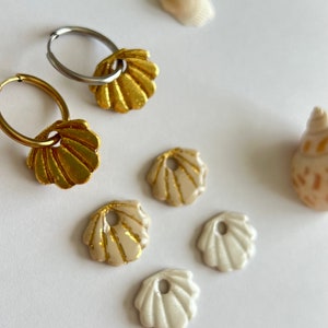 Peut inclure: Une paire de boucles d'oreilles en forme de coquille dorée avec des cercles en argent, et cinq autres breloques en forme de coquille dorée et blanche.