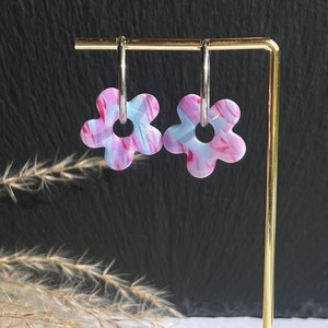 Peut inclure: Une paire de boucles d'oreilles en forme de fleur avec des tourbillons roses et bleus et des anneaux argentés.