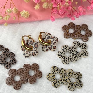 May include: Gold hoop earrings with a brown and black leopard print flower design.