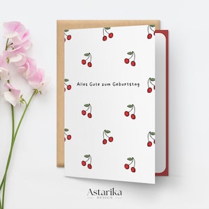 May include: A white card with a red border and a pattern of red cherries. The text "Alles Gute zum Geburtstag" is printed in black on the card.