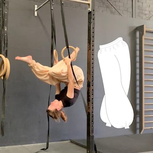 Könnte beinhalten: Eine Person, die eine gymnastische Übung an Ringen ausführt, trägt ein schwarzes Oberteil und eine hellbeige Hose. Eine Strichzeichnung einer ähnlichen Hose befindet sich rechts. Der Hintergrund umfasst Geräte und eine Wand.