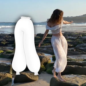 May include: White trousers with a wide leg and elastic waistband. The trousers are made of a sheer fabric and have a ruffled hem.