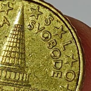 May include: Close-up of a gold coin with the word "SVOBODE" and several stars around the edge. The coin features a detailed architectural design on the left side.