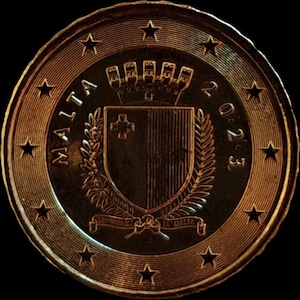 May include: A bronze coin with the word "MALTA" and the year "2023" inscribed. The coin's design includes a coat of arms with a shield, a crown, and a laurel wreath. The coin is ringed with stars.