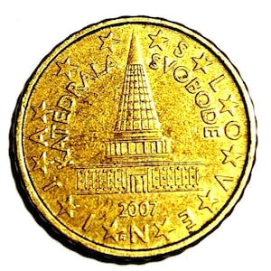 May include: A gold-coloured coin with a detailed depiction of a tall, multi-tiered structure, possibly a monument or building. The coin has text around the edges, including the year 2007. Stars are also present around the edges.