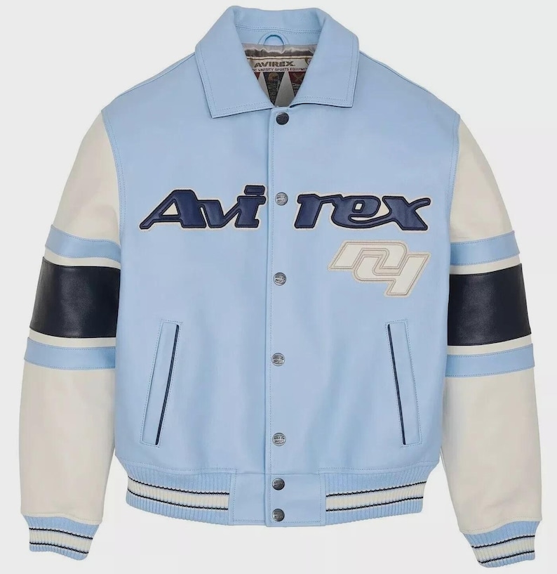May include: Light blue Avi'rex varsity jacket with white and navy blue accents. The jacket features the Avi'rex logo in navy blue and white, with a number patch. The sleeves are white with navy blue stripes. The jacket has a button-up front and two pockets.