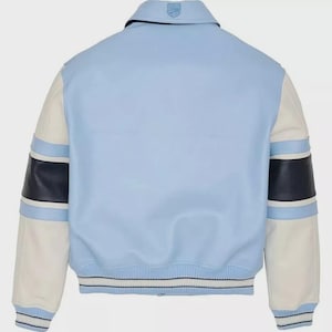 May include: Light blue varsity jacket with white sleeves and navy blue accents. The jacket features a classic collar and a striped hem. The sleeves have navy blue and light blue stripes. A logo is visible on the back of the collar.