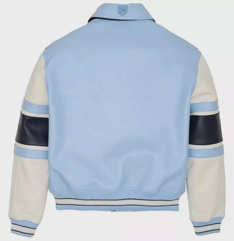 May include: Light blue varsity jacket with white sleeves and navy blue accents. The jacket features a classic collar and a striped hem. The sleeves have navy blue and light blue stripes. A logo is visible on the back of the collar.
