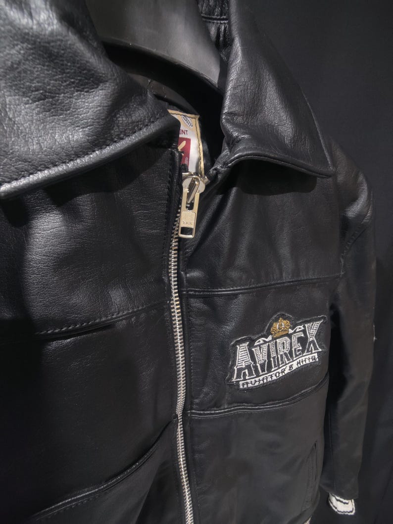 Puede incluir: Chaqueta de cuero negro con cremallera plateada y cuello con solapas. La chaqueta presenta el logotipo bordado "AVIREX" en el pecho. La chaqueta tiene un dise&ntilde;o cl&aacute;sico.