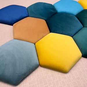 May include: A selection of hexagon-shaped cushions in shades of blue, teal, yellow, and brown. The cushions are arranged in a cluster, creating a pattern. The soft, plush texture is visible. The cushions are made of a soft material.