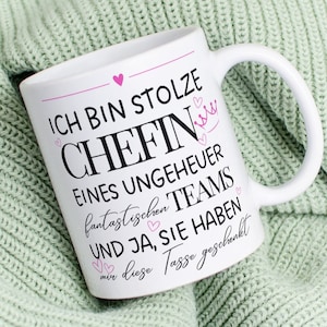 Peut inclure: Une tasse en céramique blanche avec un motif de cœur et de couronne rose. La tasse a un texte noir qui dit "Ich bin stolze Chefin eines ungeheuer fantastischen Teams und ja, sie haben mir diese Tasse geschenkt."