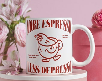 May include: White ceramic mug with a red design that says "More Espresso Less Depresso" and features a cartoon coffee cup with a smiling face. The mug is sitting on a pink and white box.