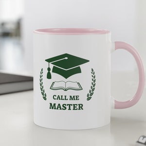 Puede incluir: Taza de cerámica blanca con borde y asa de color rosa. La taza presenta un diseño verde de gorro de graduación, libro y corona de laurel. El texto "CALL ME MASTER" está impreso debajo del diseño.