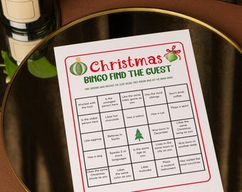 May include: A white Christmas Bingo game card with a green and red border. The card features the text "Christmas Bingo Find the Guest" and various prompts for players to find guests who match the descriptions. The card is on a gold-colored tray.