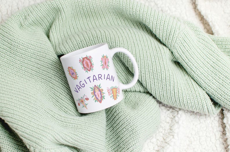 May include: White ceramic mug with a pink, purple, and orange floral design and the word "Vagitarian" in purple lettering.