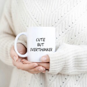 May include: White ceramic mug with black text that reads "Cute but Overthinker".