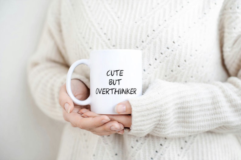 May include: White ceramic mug with black text that reads "Cute but Overthinker".