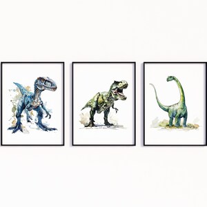 Puede incluir: Tres acuarelas de dinosaurios en marcos negros. La primera pintura presenta un velociraptor azul, la segunda un Tyrannosaurus Rex verde y la tercera un Brachiosaurus verde.