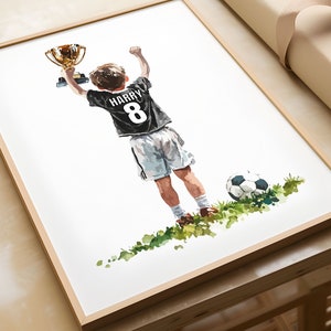 May include: A watercolour painting of a young person holding up a gold trophy, wearing a black football shirt with the name "HARRY" and the number "8" on the back. The person is standing on a green field with a football nearby.