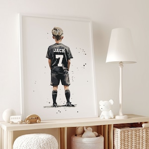 K&ouml;nnte beinhalten: Eine Schwarzwei&szlig;illustration eines jungen Jungen, der ein schwarzes Fu&szlig;balltrikot mit dem Namen "JACK" und der Nummer "7" auf dem R&uuml;cken tr&auml;gt. Der Junge steht mit den H&auml;nden in den Taschen und blickt vom Betrachter weg.