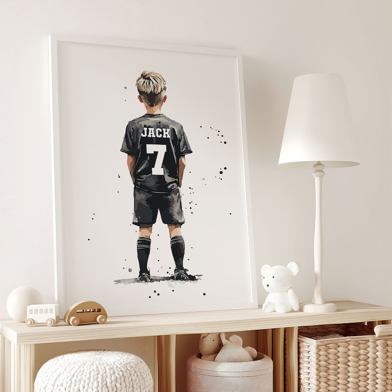 K&ouml;nnte beinhalten: Eine Schwarzwei&szlig;illustration eines jungen Jungen, der ein schwarzes Fu&szlig;balltrikot mit dem Namen "JACK" und der Nummer "7" auf dem R&uuml;cken tr&auml;gt. Der Junge steht mit den H&auml;nden in den Taschen und blickt vom Betrachter weg.