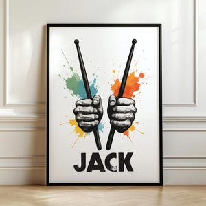 May include: Framed art print showing two hands gripping drumsticks, set against colourful paint splashes. The word "JACK" is printed in bold, black letters at the bottom of the print.