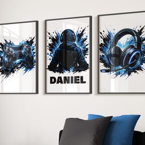 May include: Three framed art prints with gaming themes. The set includes a black and blue games controller, a gamer with the name "DANIEL", and a gaming headset. Each print has a blue and black splatter effect on a white background.