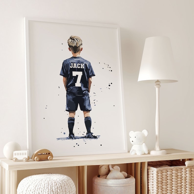 K&ouml;nnte beinhalten: Ein Aquarellbild eines jungen Jungen, der ein blaues Fu&szlig;balltrikot mit dem Namen "JACK" und der Nummer "7" auf dem R&uuml;cken tr&auml;gt. Der Junge steht mit dem R&uuml;cken zum Betrachter und blickt nach links.
