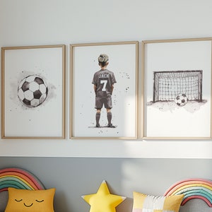 K&ouml;nnte beinhalten: Drei gerahmte Aquarell-Illustrationen eines Fu&szlig;ballspielers, eines Fu&szlig;balls und eines Fu&szlig;balltors. Der Spieler tr&auml;gt ein graues Trikot mit dem Namen "Jack" und der Nummer "7" auf dem R&uuml;cken. Der Fu&szlig;ball ist schwarz-wei&szlig;. Das Fu&szlig;balltor ist schwarz-wei&szlig; mit einem wei&szlig;en Netz.