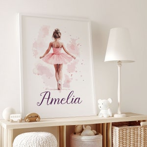 May include: A watercolour painting of a young ballerina wearing a pink tutu and pointe shoes. The background is a soft pink with watercolour splatters. The name Amelia is written in purple script at the bottom of the painting.