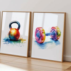May include: Two framed watercolor paintings of colorful gym equipment. The first painting shows a kettlebell with a rainbow color scheme. The second painting shows a dumbbell with a rainbow color scheme.