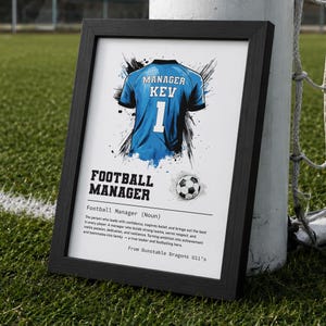 May include: A framed print featuring a blue jersey graphic with the text MANAGER KEV 1, a football, and the definition of a football manager. The text includes the phrase Football Manager (Noun) and From Dunstable Dragons U11's.