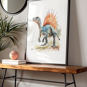 Puede incluir: Impresi&oacute;n en acuarela enmarcada de un dinosaurio Spinosaurus. La obra de arte presenta un dinosaurio azul y gris con una vela naranja y roja. La impresi&oacute;n enmarcada se exhibe en un banco de madera.