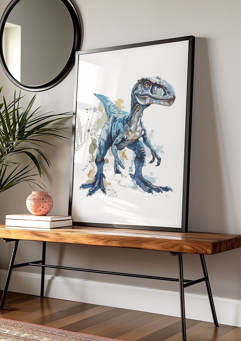 Puede incluir: Un cuadro enmarcado con una ilustraci&oacute;n de acuarela de un dinosaurio azul. La obra de arte tiene un fondo blanco con salpicaduras de pintura azul y verde. El cuadro con marco negro se exhibe sobre un banco de madera.