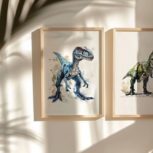 Puede incluir: Dos pinturas de acuarela enmarcadas de dinosaurios. La pintura de la izquierda presenta un velociraptor azul con salpicaduras de acuarela en el fondo. La pintura de la derecha presenta un Tyrannosaurus Rex verde con salpicaduras de acuarela en el fondo.