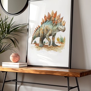 Puede incluir: Impresi&oacute;n en acuarela de un dinosaurio Estegosaurio en tonos verdes, naranjas y marrones, enmarcada en negro. La obra de arte se exhibe sobre un banco de madera con patas de metal negro, junto a un jarr&oacute;n decorativo y libros.