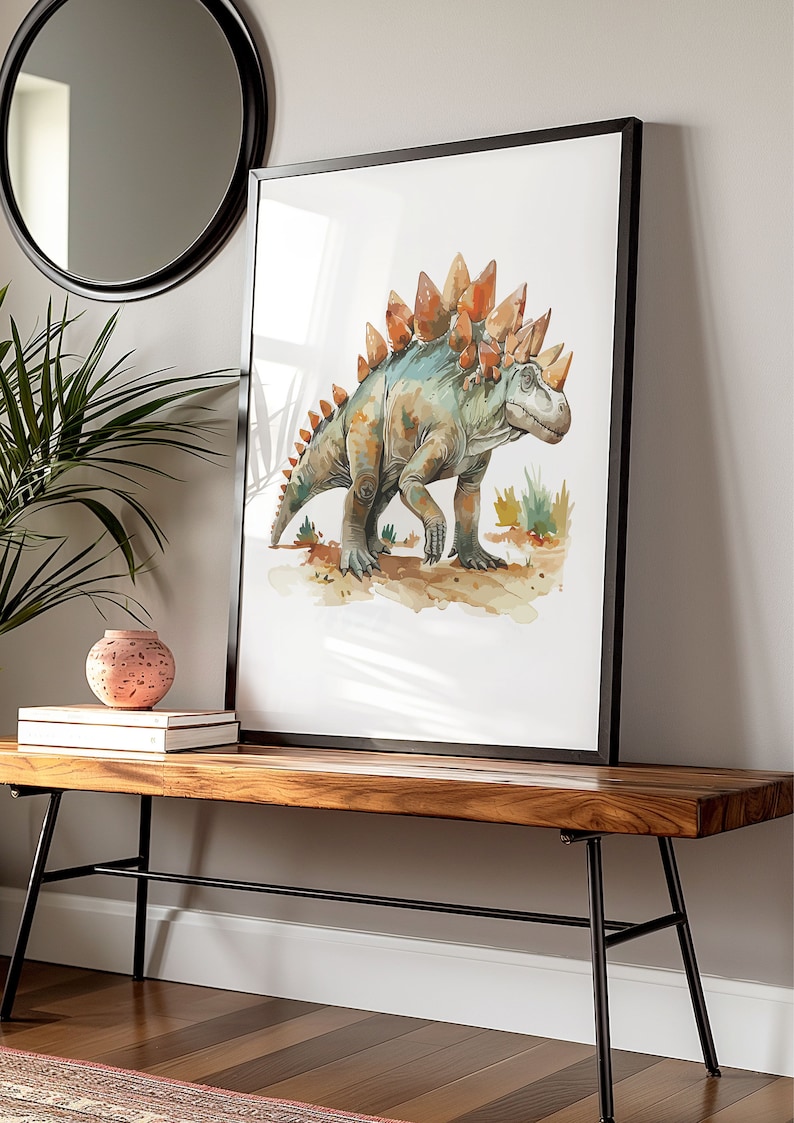 Puede incluir: Impresi&oacute;n en acuarela de un dinosaurio Estegosaurio en tonos verdes, naranjas y marrones, enmarcada en negro. La obra de arte se exhibe sobre un banco de madera con patas de metal negro, junto a un jarr&oacute;n decorativo y libros.