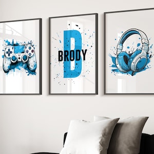 May include: Three framed art prints with gaming designs. One shows a blue and white games controller, another displays the name "BRODY" with a blue "B", and the third depicts blue and white headphones. All prints have a white background.
