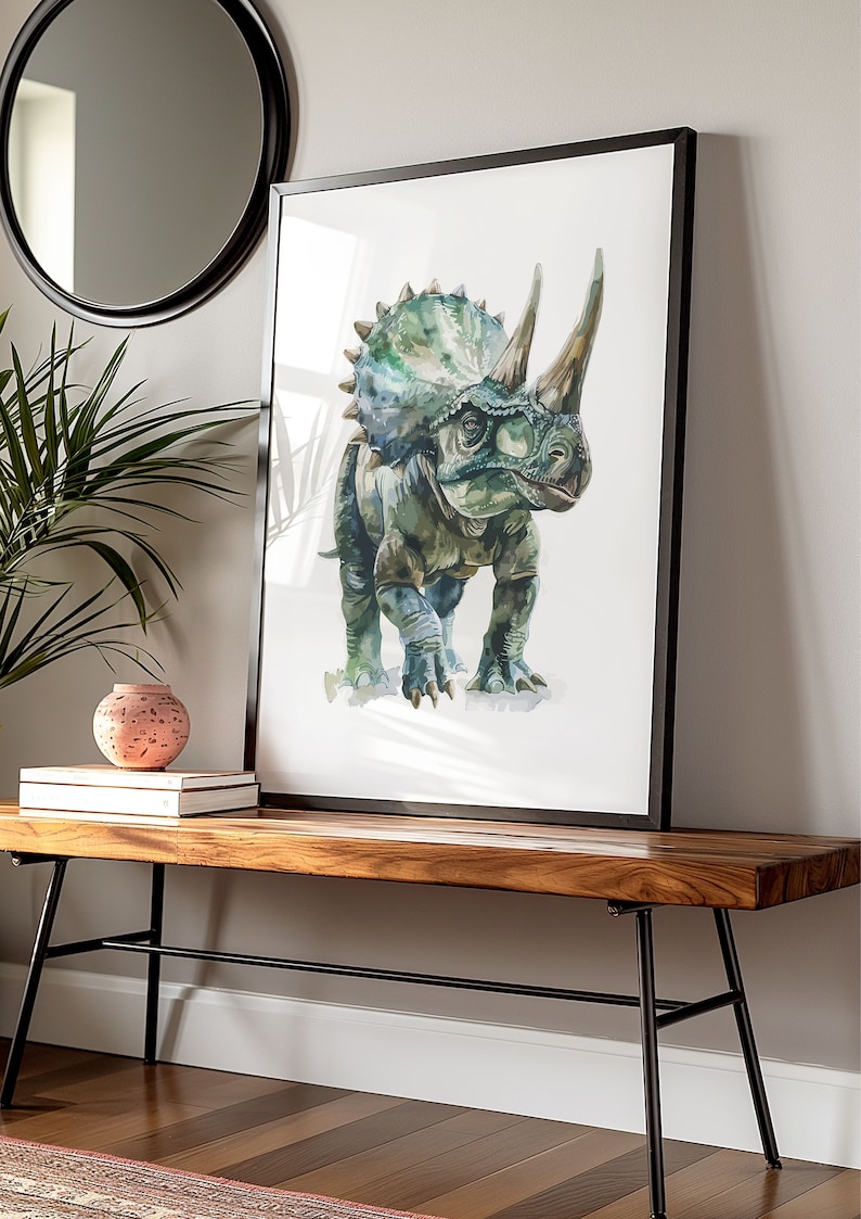 Puede incluir: Impresi&oacute;n en acuarela de un dinosaurio Triceratops en tonos verdes y azules, enmarcada en negro. La obra de arte se exhibe sobre un banco de madera con patas de metal negro, junto a un jarr&oacute;n decorativo y libros. Un espejo redondo cuelga en la pared.