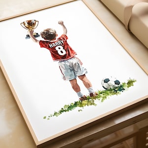 May include: A watercolour painting of a young football player holding up a trophy. The player is wearing a red jersey with the name "HARRY" and the number "8" on the back. The player is standing on a green pitch with a football.