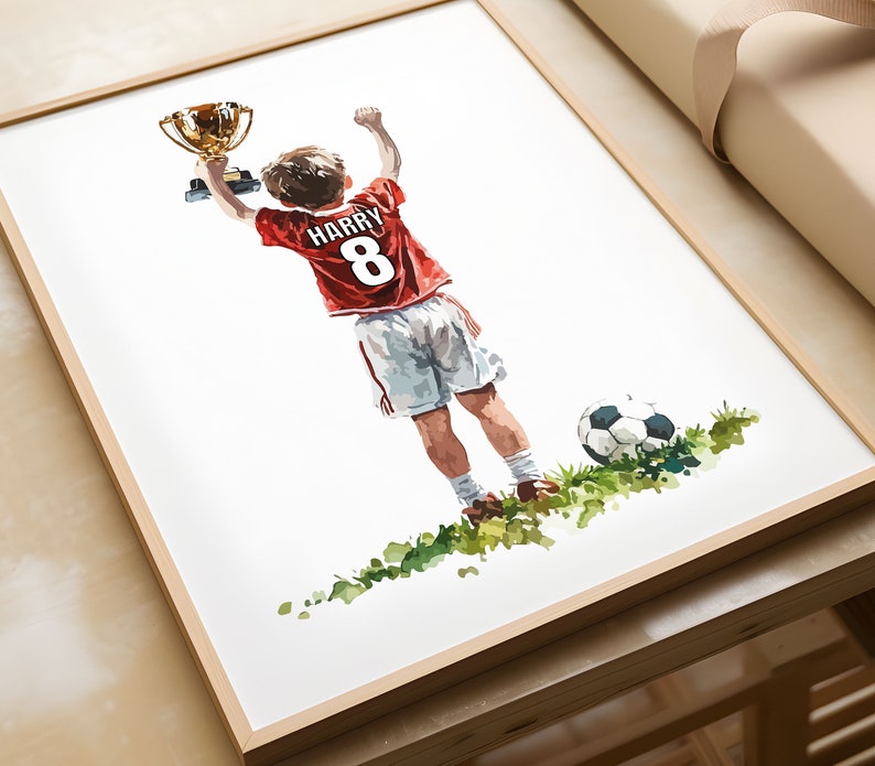 May include: A watercolour painting of a young football player holding up a trophy. The player is wearing a red jersey with the name "HARRY" and the number "8" on the back. The player is standing on a green pitch with a football.