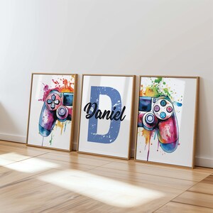 May include: Three framed prints featuring a watercolour design of a colourful video game controller. The middle print has the name "Daniel" in a blue box.