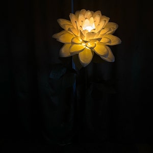 Puede incluir: Una l&aacute;mpara de papel con forma de flor blanca con una bombilla de luz blanca c&aacute;lida. La l&aacute;mpara est&aacute; sobre un soporte negro y tiene un cable blanco.